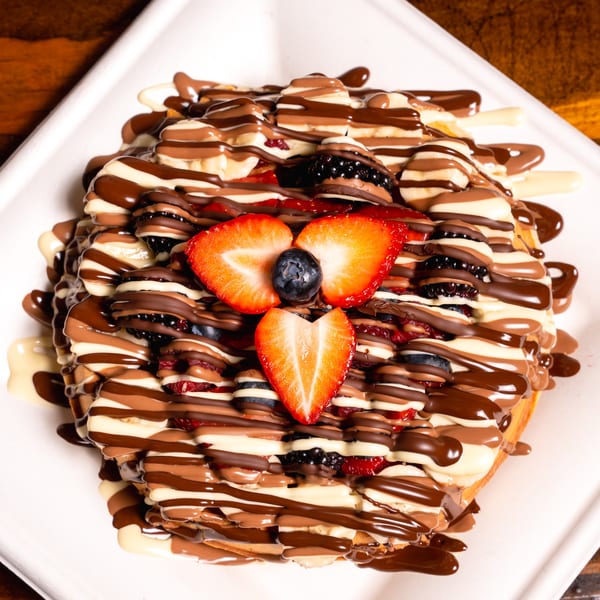 Waffle topped with strawberries, blueberries, bananas, and drizzled with milk, white, and dark chocolate.