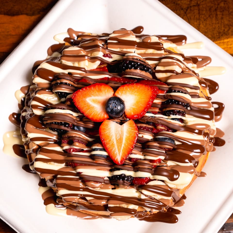 Waffle topped with strawberries, blueberries, bananas, and drizzled with milk, white, and dark chocolate.