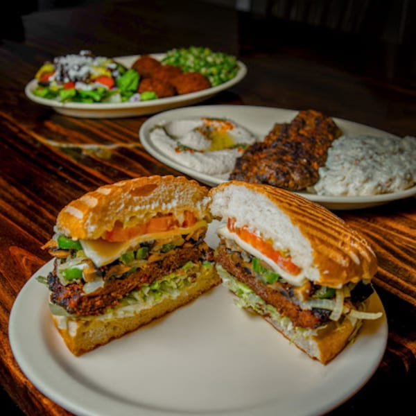A grilled sandwich cut in half, with plates of Mediterranean food in the background.