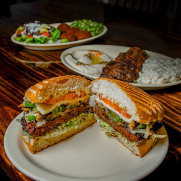 A cut panini sandwich with vegetables and meat, with other Mediterranean dishes blurred in the background.