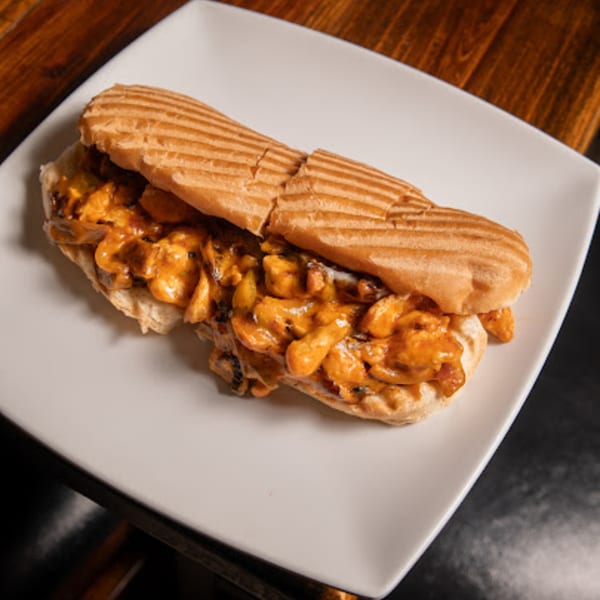 A grilled Mediterranean chicken sandwich with creamy orange sauce on a white rectangular plate.