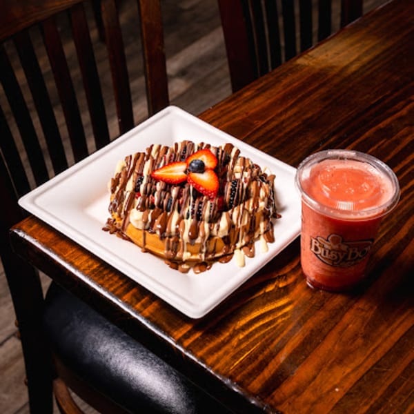 Waffle with chocolate, bananas, strawberries, and blueberries, next to a Busy Boy smoothie.