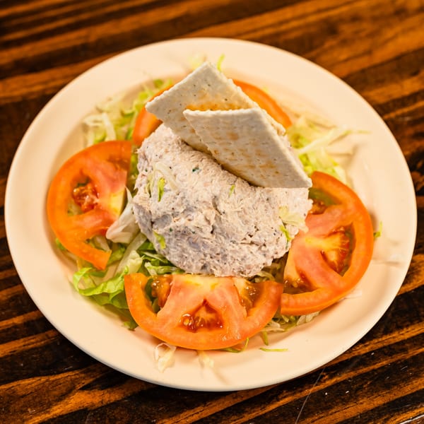 Tuna salad with crackers, lettuce, and tomato slices on a white plate at Busy Boy Mediterranean Grill.