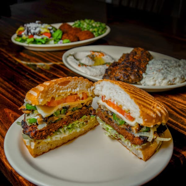 A cut Mediterranean sandwich on a white plate, with other dishes blurred in the background.