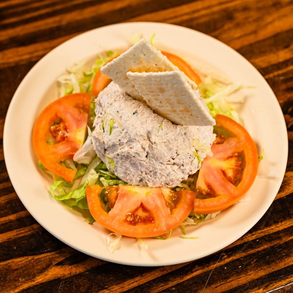 Tuna salad with crackers, lettuce, and tomato slices on a white plate at Busy Boy Mediterranean Grill & Cafe.