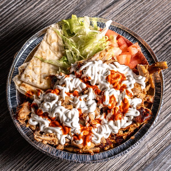Mediterranean chicken and rice platter with white and red sauce, pita bread, lettuce, and tomatoes.