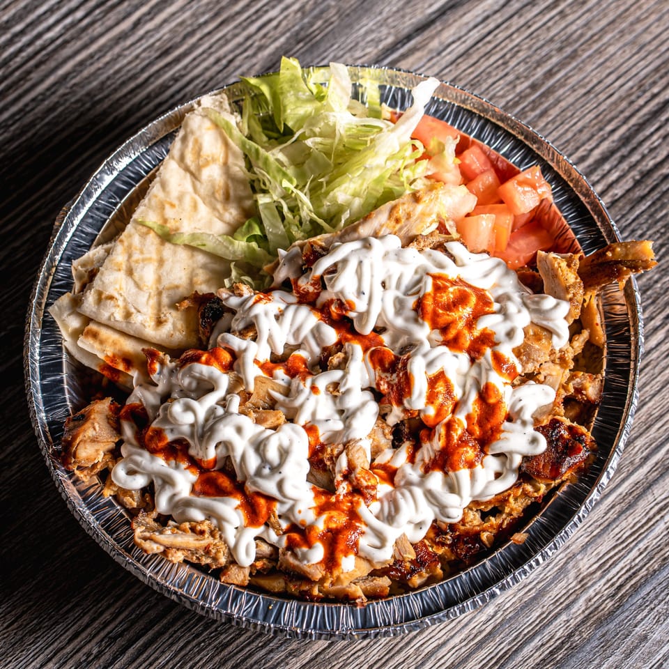 Mediterranean chicken and rice platter with white and red sauce, pita bread, lettuce, and tomatoes.