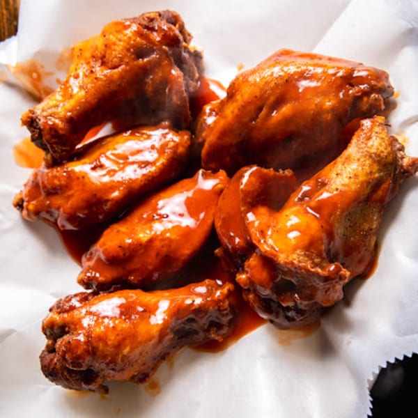 Six saucy chicken wings, glistening with a rich red glaze, served on white parchment paper.