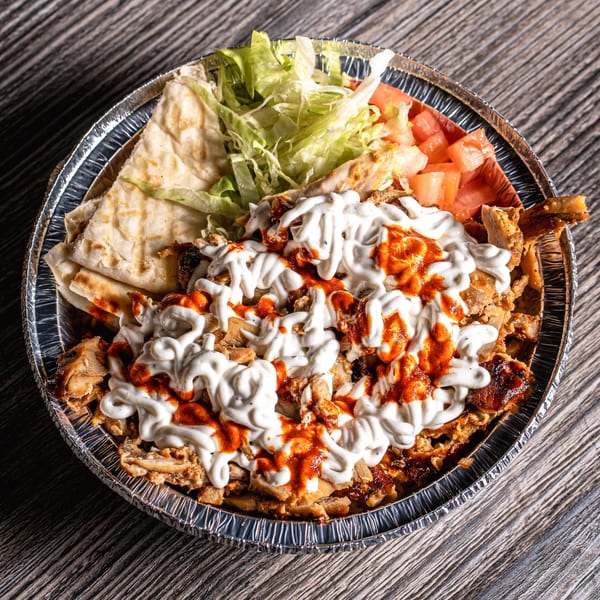 Mediterranean chicken shawarma platter with white and red sauce, pita bread, lettuce, and diced tomatoes.