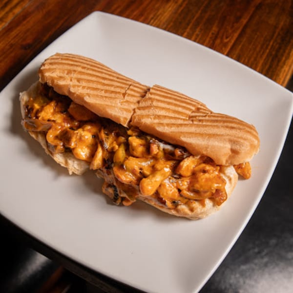 A grilled Mediterranean chicken sandwich with creamy orange sauce and mushrooms on a white plate.