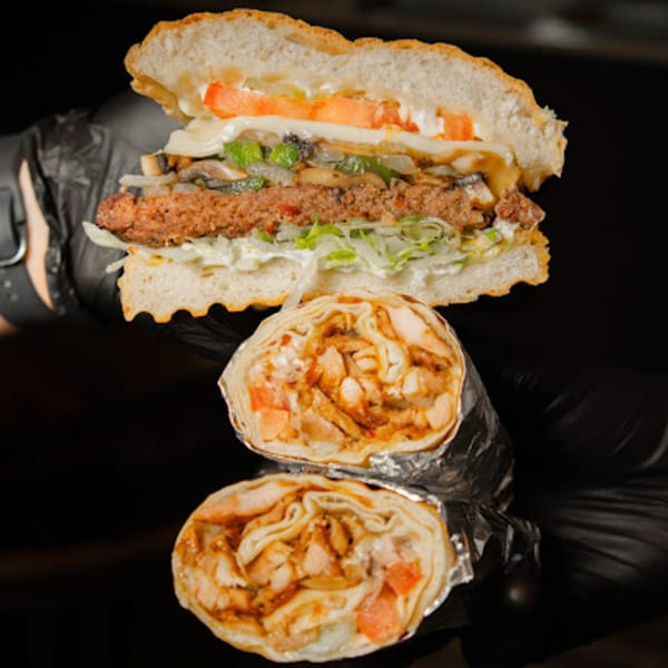 A Mediterranean burger with vegetables and two chicken shawarma wraps, held by gloved hands.