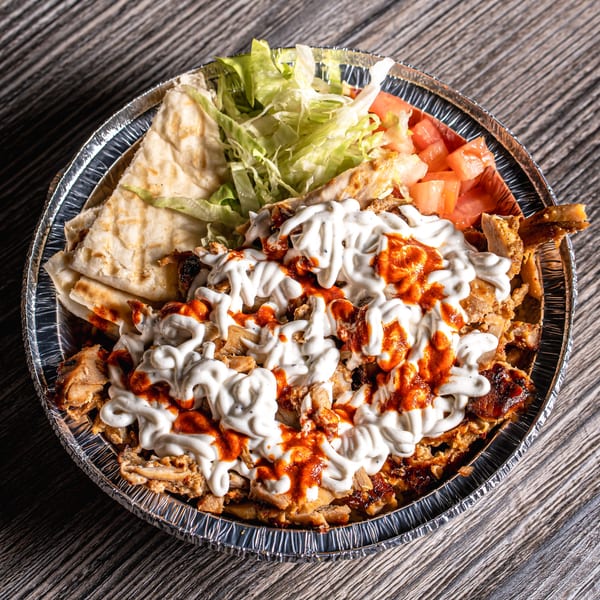 Mediterranean chicken shawarma platter with white and red sauce, pita bread, lettuce, and tomatoes.