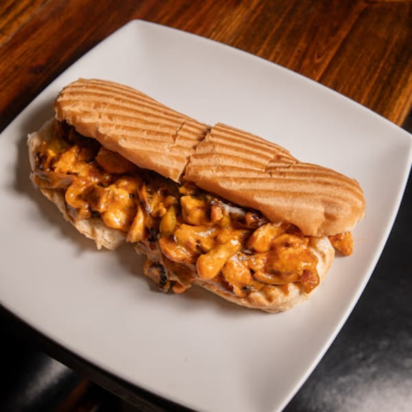 A grilled Mediterranean chicken sandwich with creamy orange sauce on a white rectangular plate.